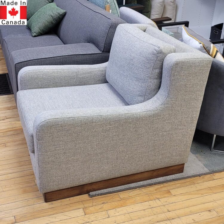 Light grey accent chair with sloped arm and deep seat. On wood legs in walnut stain.